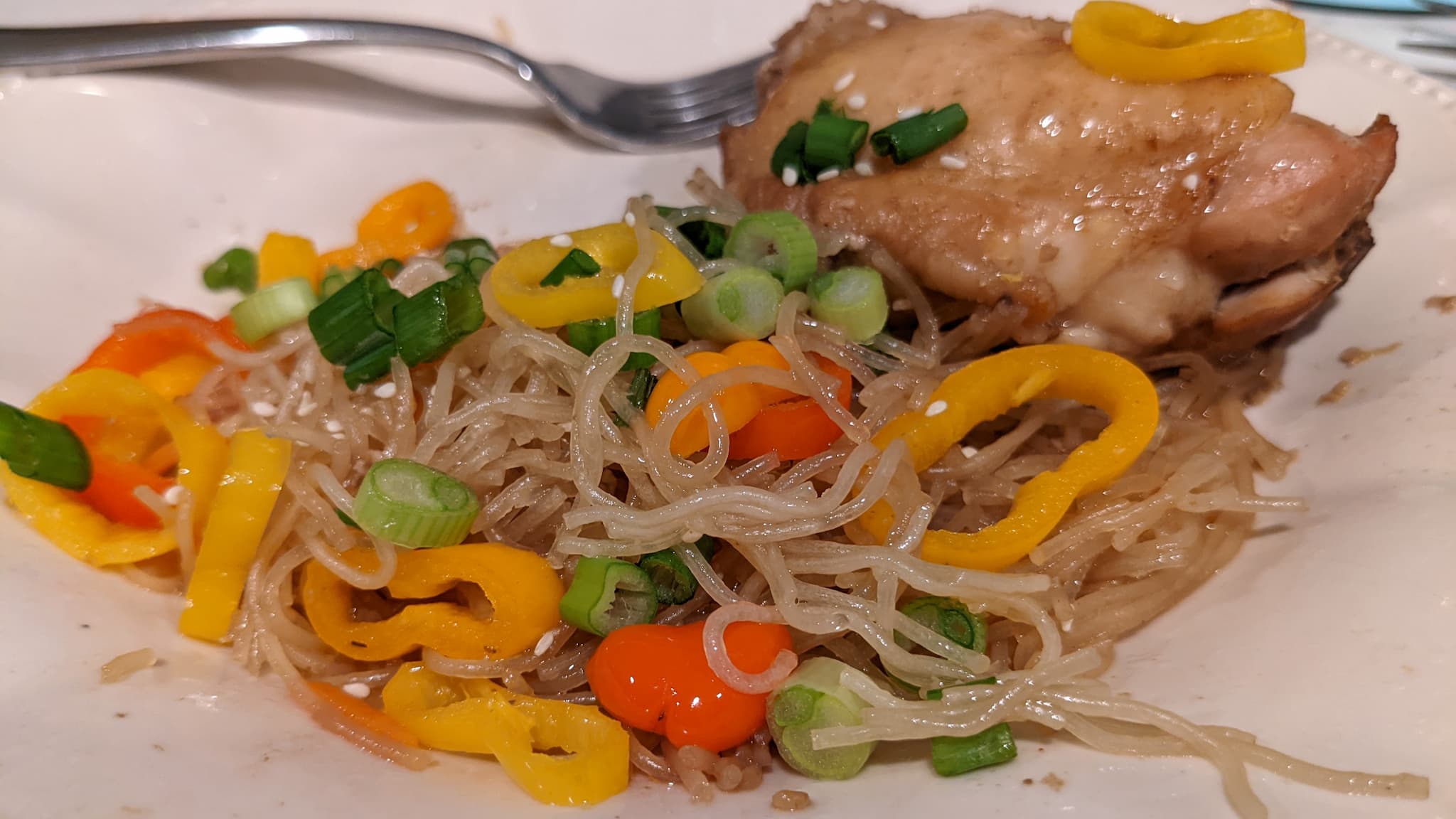 plate with noodles, colorful peppers, green onions, and a piece of roasted chicken.